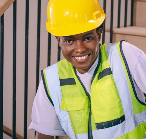 Confident construction worker wearing a hardhat and reflective vest while seated indoors.